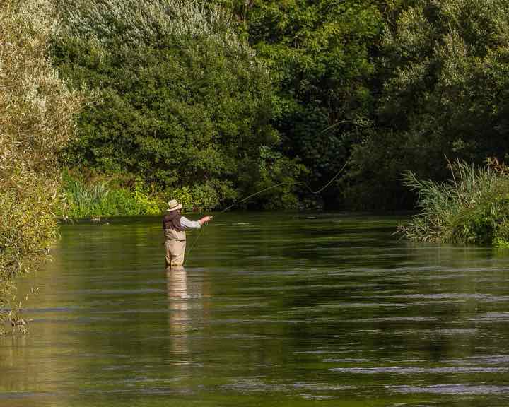 An angler wading a clear river with a fly rod